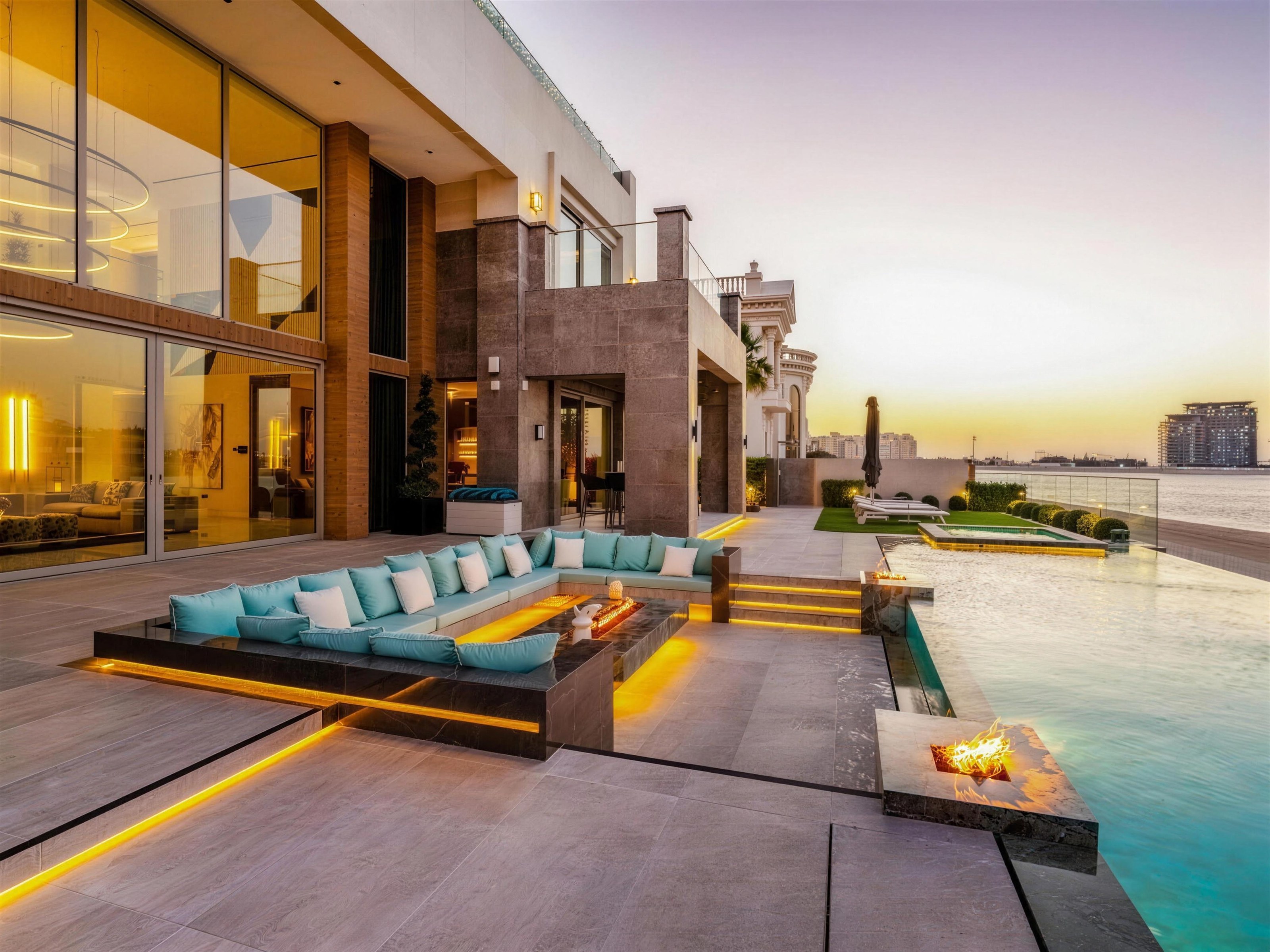 Waterfront villa terrace with a sunken lounge, fire pit and infinity pool at sunset